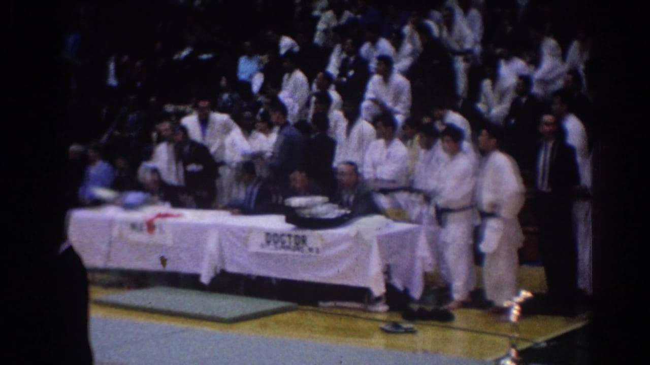 White-gi competitors and suited officials stand near the DOCTOR table at a 1967 Los Angeles indoor karate tournament.