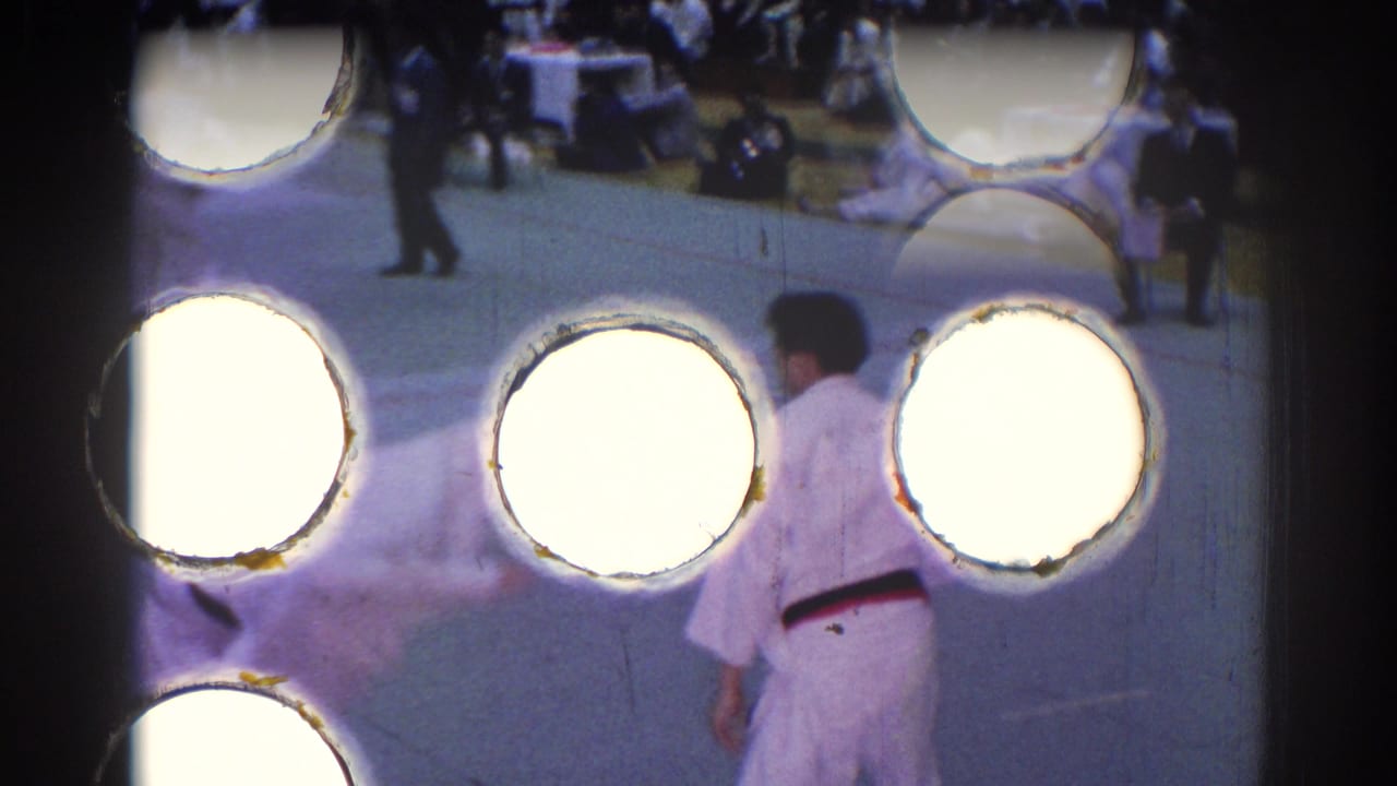 Judo competitor seen near large bright film perforation artifacts at the frame edge.