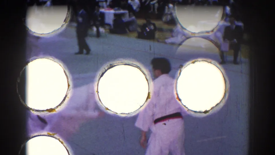 1967 Los Angeles judo footage partially obscured by bright film perforation artifacts, with a competitor in a white gi visible on the mat.