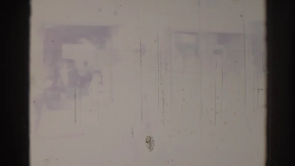 Faded 8mm frame with indistinct figures or interior shapes, heavy exposure wash, and visible vertical scratches.