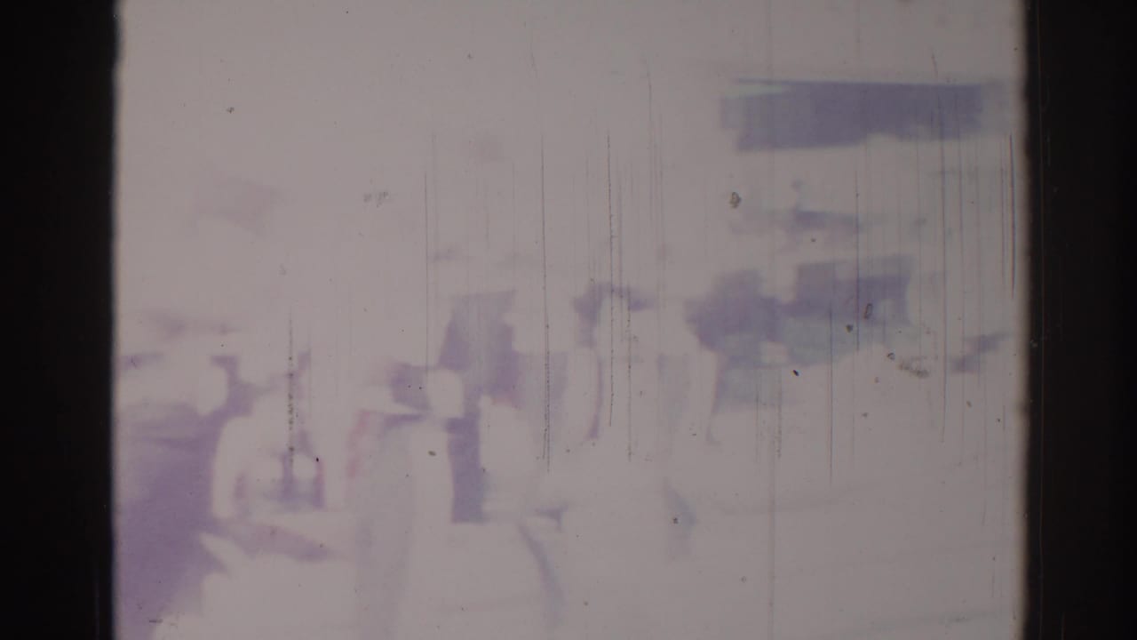 Faint figures and possible parade movement visible through pale, scratched film damage.