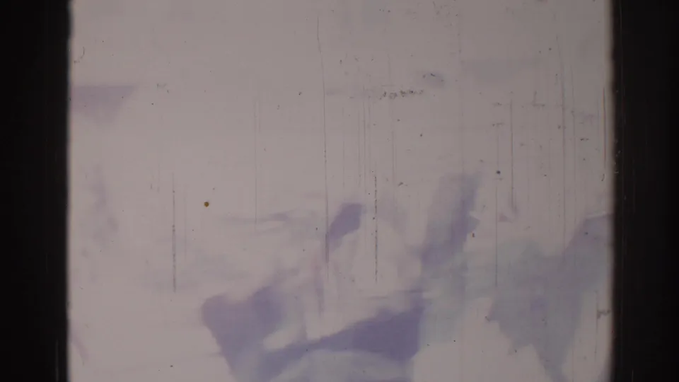 Damaged 8mm frame from the 1967 Los Angeles clip with blurred silhouettes near the lower edge and strong purple fading.