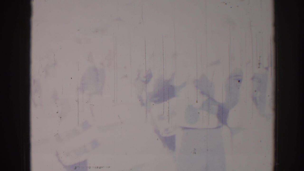 Severely faded frame with faint parade figures behind scratches and dark film borders.