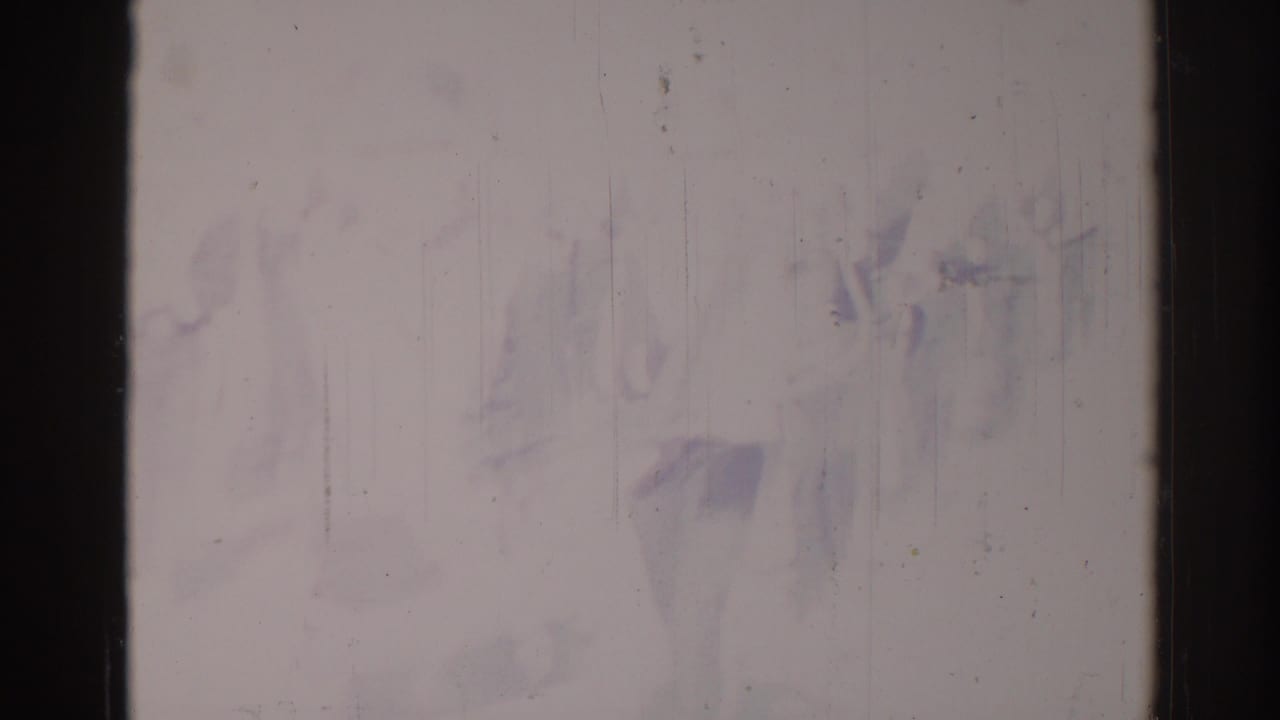 Faded scratched frame with indistinct figures moving through the center area.