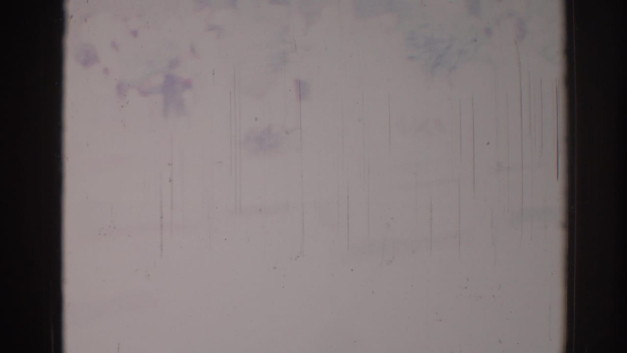 Damaged film frame with dark vertical border, pale surface, scratches, and faint stains.