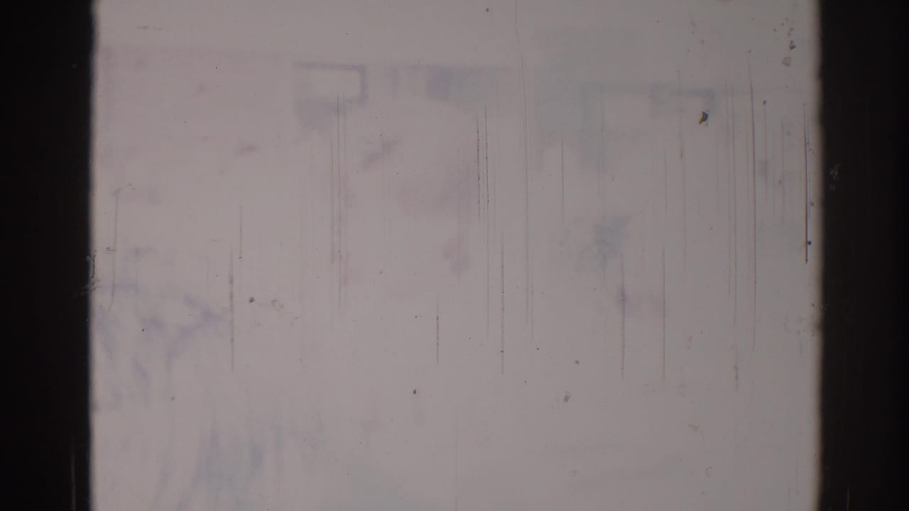 Overexposed 8mm frame with black borders, scratches, dust, and faint blue-purple staining.