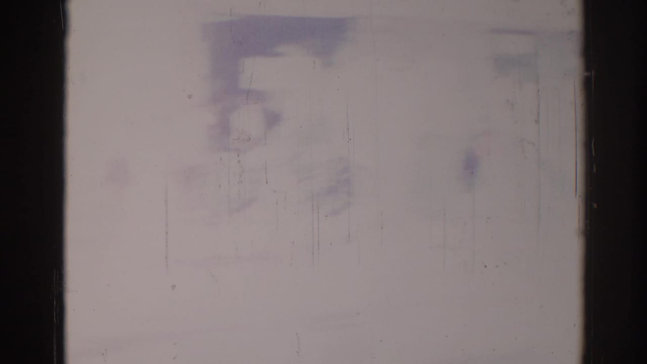 Washed-out film frame with dark side borders, vertical scratches, and pale purple marks near the top.