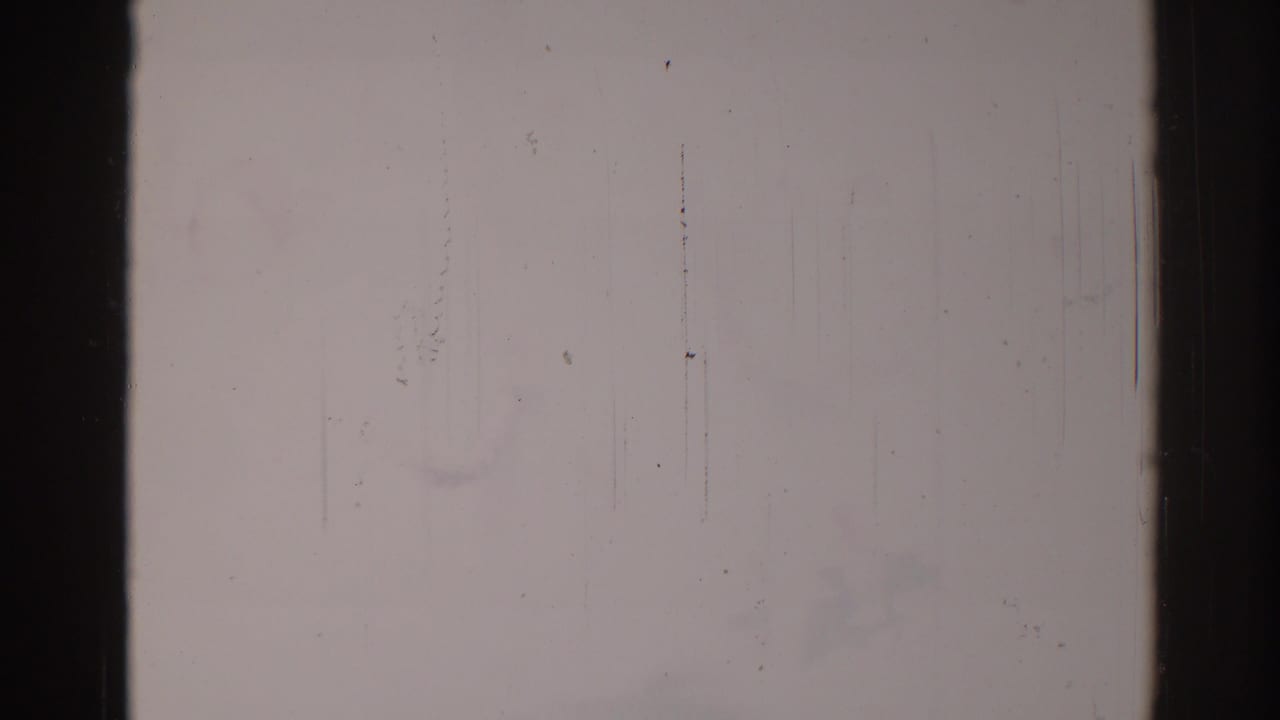 Mostly blank faded film frame with scratches and dark frame edges.