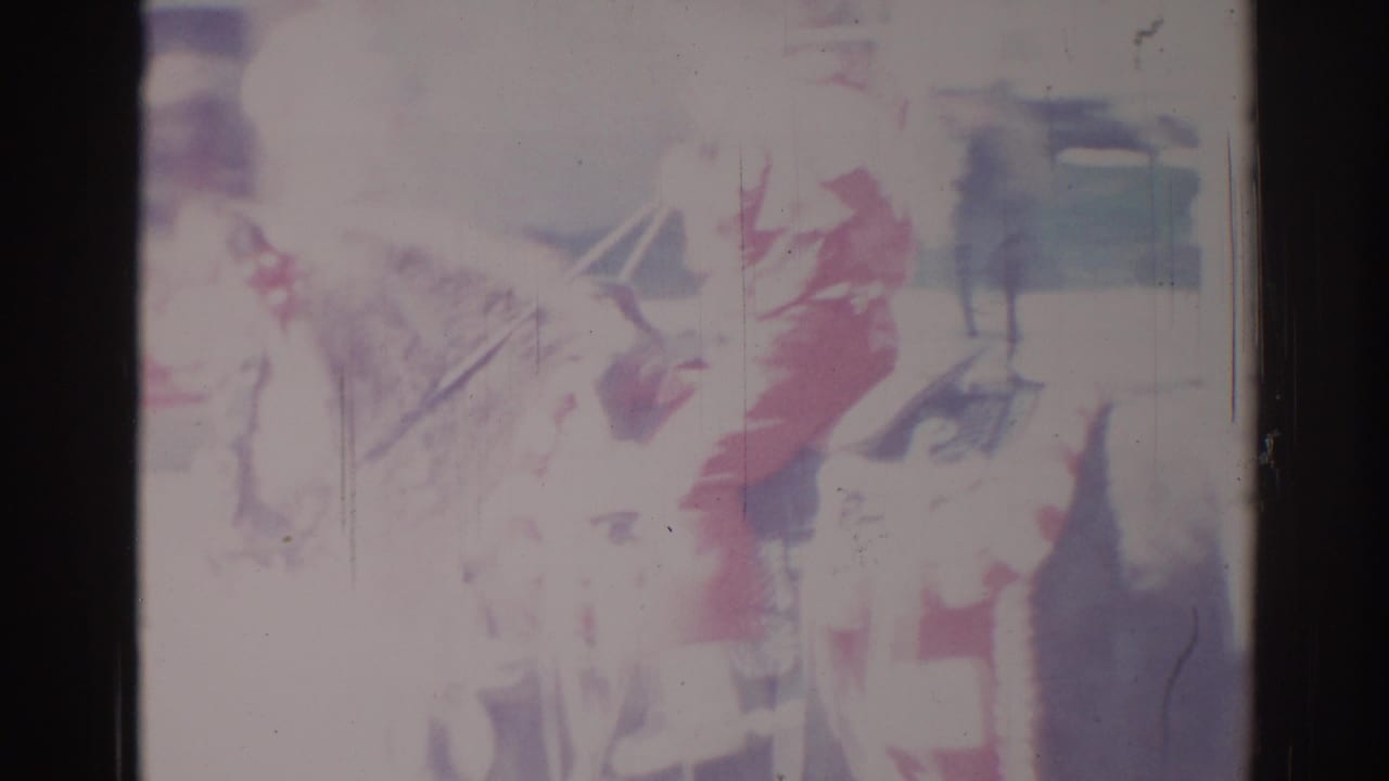 Faded parade scene with a mounted figure or rider, decorations, and dark film edges.