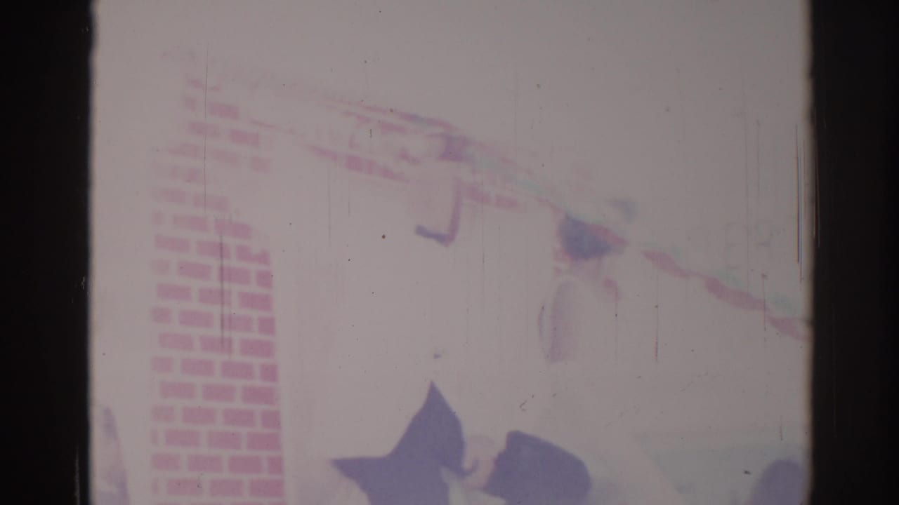 Overexposed parade decorations near a brick-patterned wall and dark film frame edge.