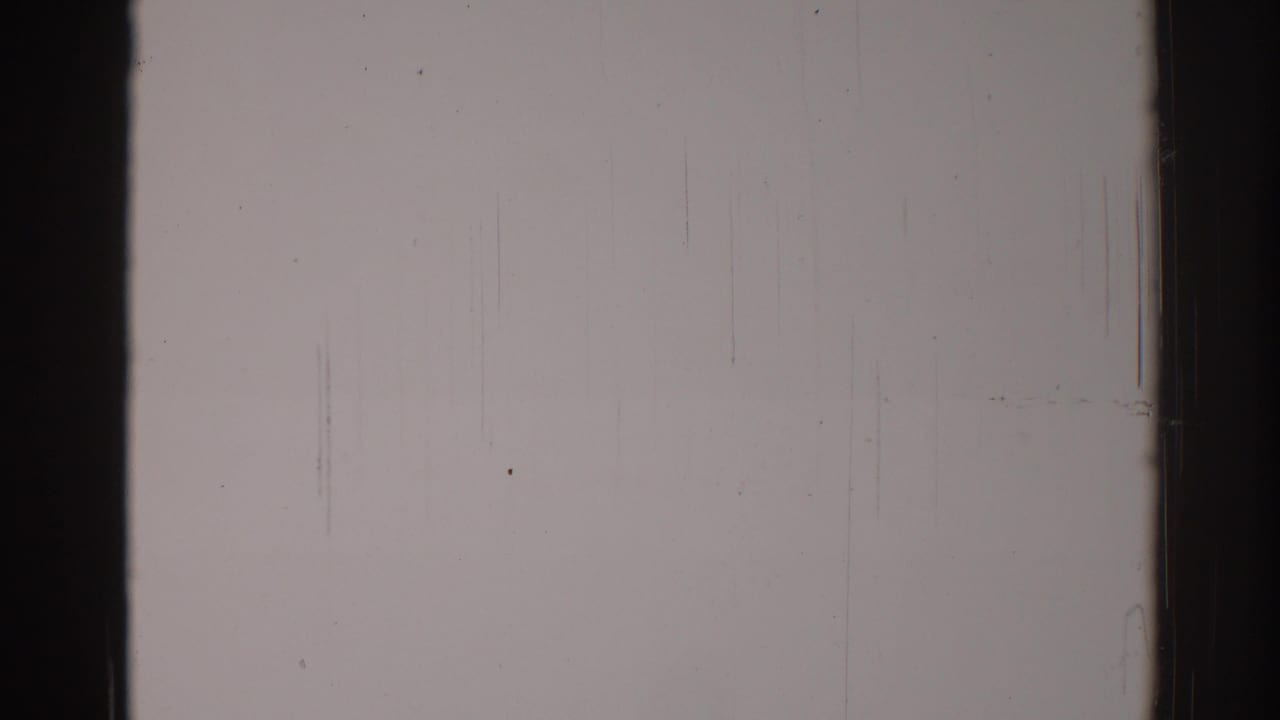 Pale wall with dark film borders, light grain, dust specks, and fine vertical scratches.