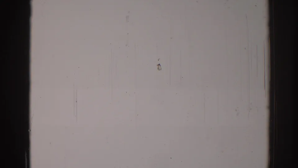 1967 Los Angeles 8mm frame of a blank pale wall with dark gate edges, scattered dust, fine scratches, and a small yellowish smudge.
