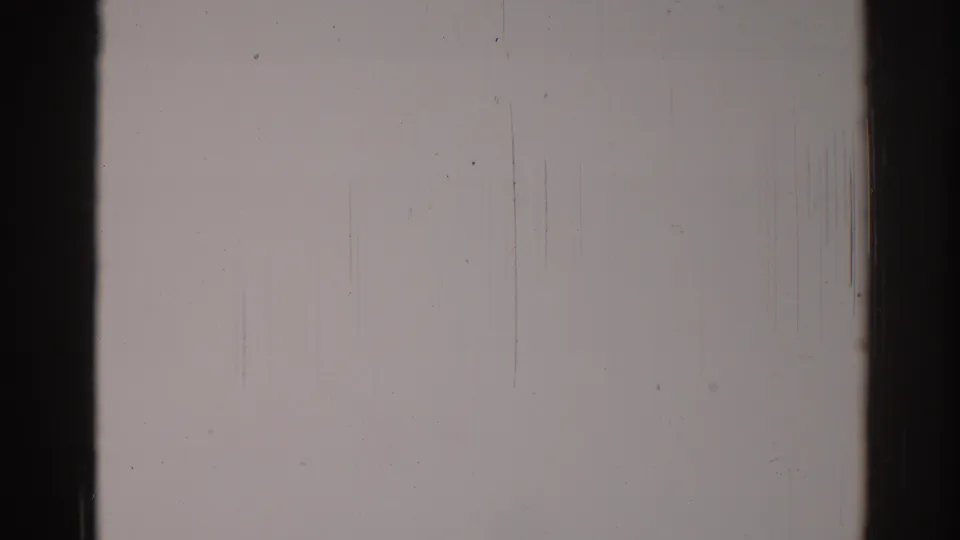 1967 Los Angeles 8mm frame of a pale wall with black frame edges, fine vertical abrasion, dust, grain, and slight exposure variation.