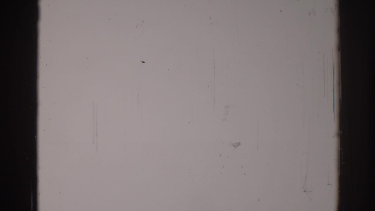 Pale 8mm film frame with dark borders, dust specks, scratches, and a vertical dark band.