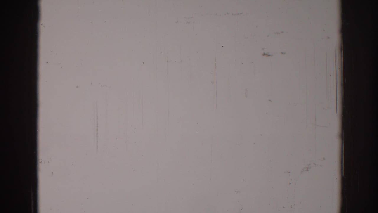 Light gray film surface with vertical scratches, dust, dark edge borders, and subtle exposure variation.