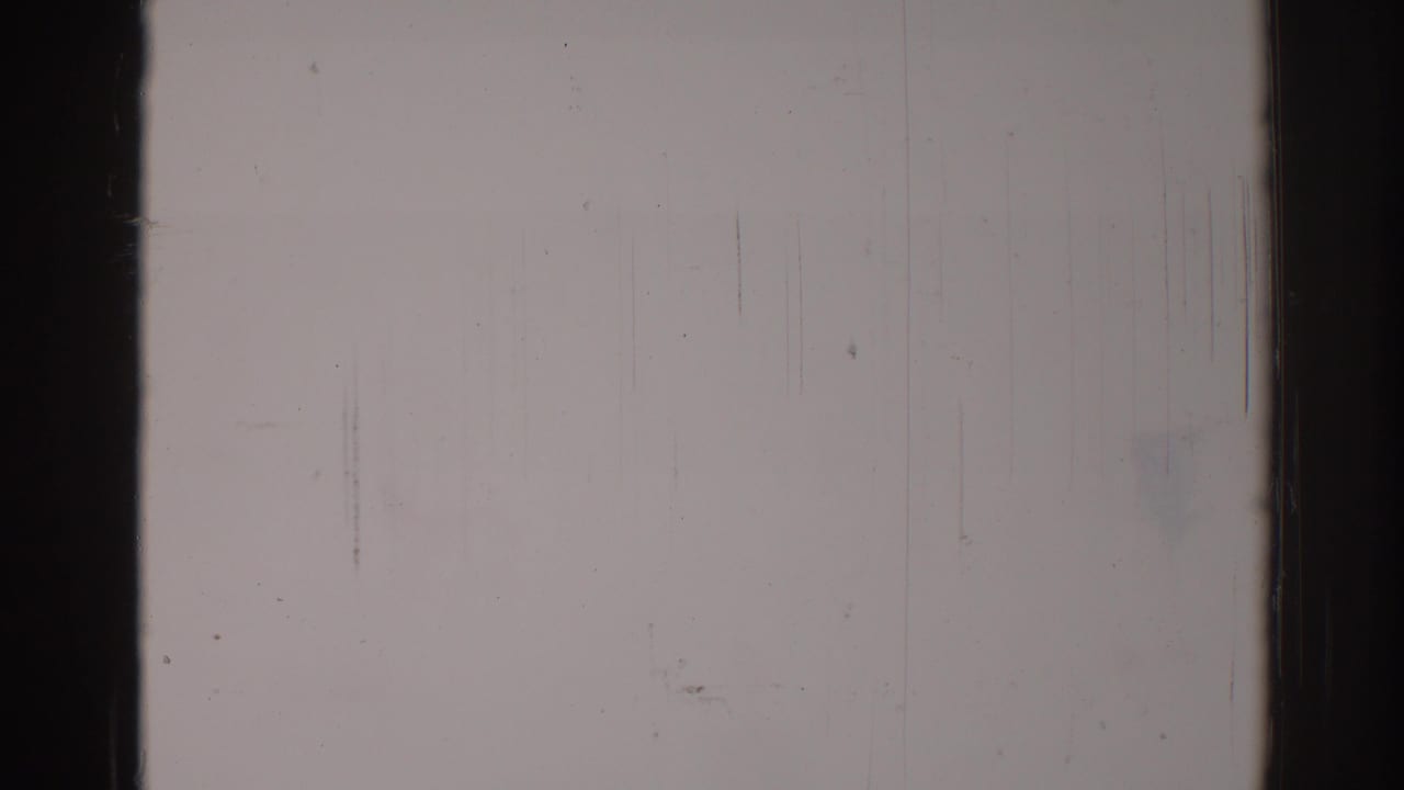 Blank pale 8mm film frame with dark vertical borders, scratches, dust specks, and grain.