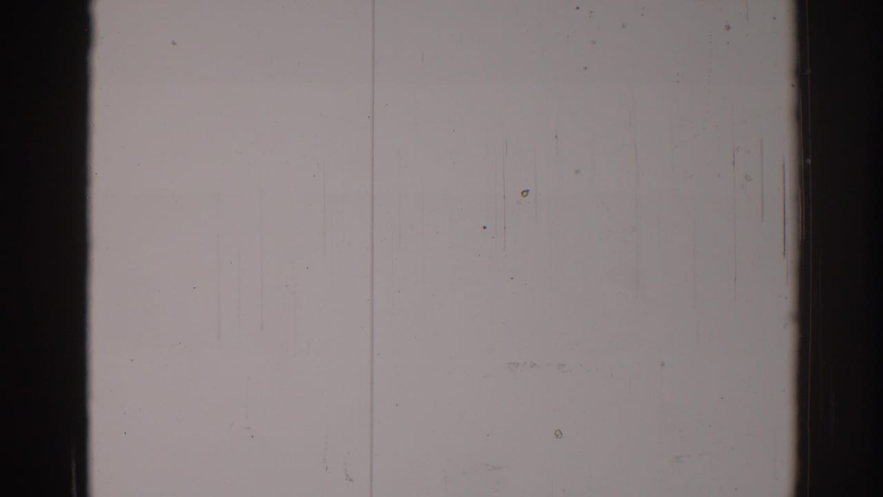 Blank film frame divided by a dark vertical band, with faint scratches, specks, and grain.
