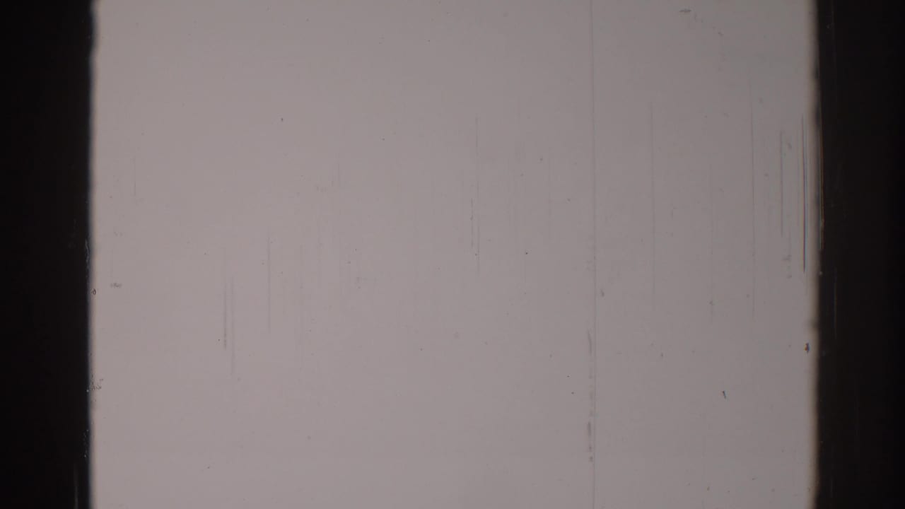 Blank pale film frame with dark edge bars, scratches, dust specks, and grain.