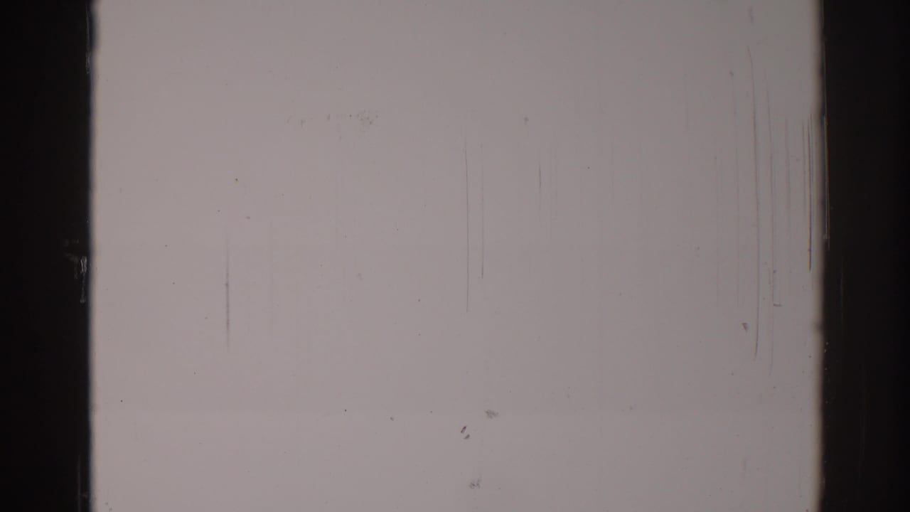 Blank pale film frame with dark vertical borders, dust specks, scratches, and a horizontal scan band.