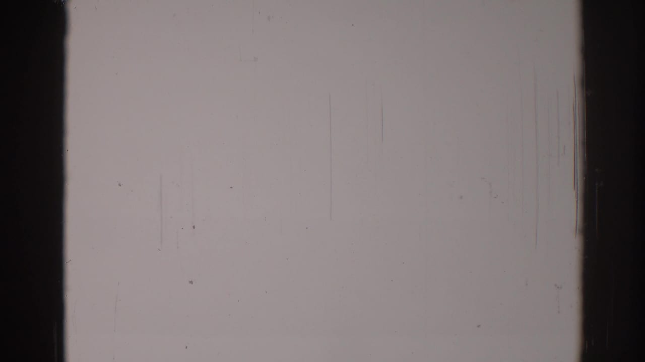 Blank film area with dark frame edge, vertical scratches, scattered dust, and muted gray exposure.