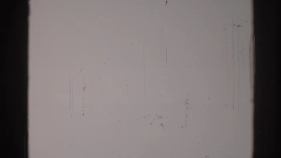 1967 Los Angeles 8mm blank frame showing dark film border, pale stock surface, dust deposits, vertical scratches, and grain texture.