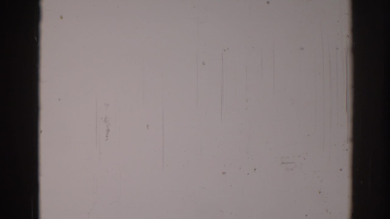 Pale gray scratched film frame with dark vertical borders and scattered dust specks.
