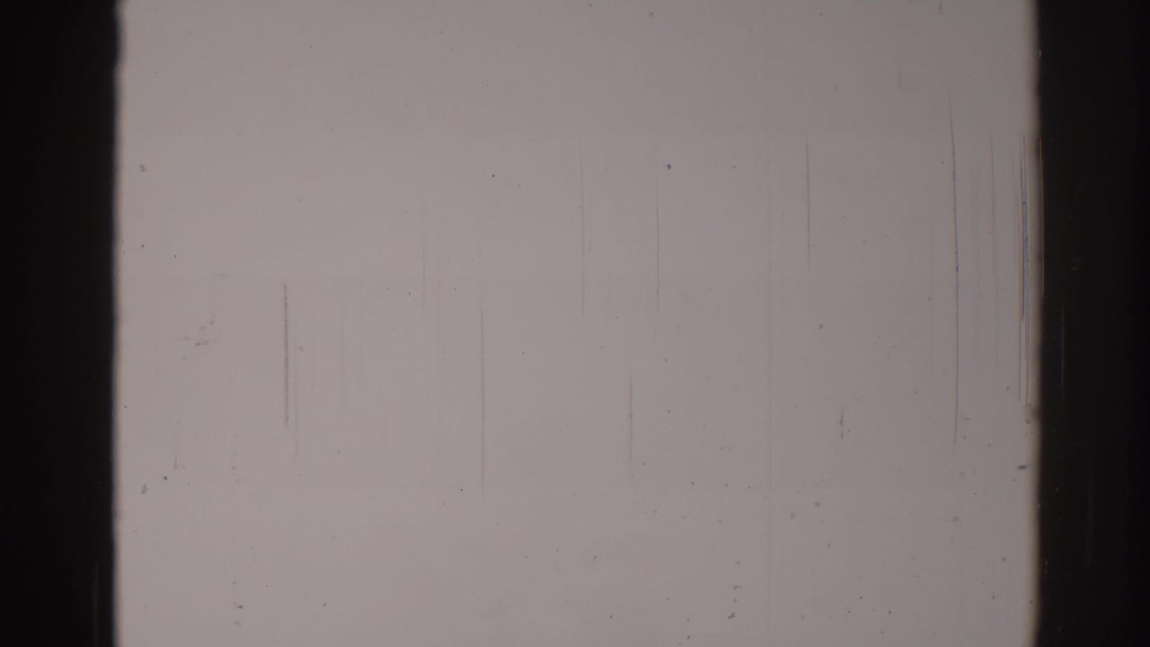 Overexposed 8mm frame with no identifiable subject, bordered by dark film edges and marked by vertical scratches and dust.