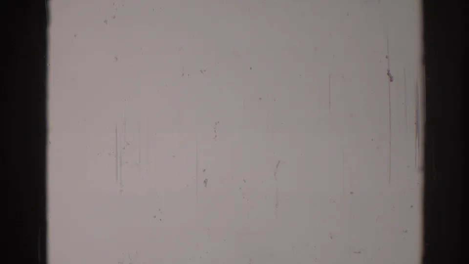 Nearly blank overexposed 8mm frame, with dark borders, vertical scratches, dust specks, and no visible people or landmarks.