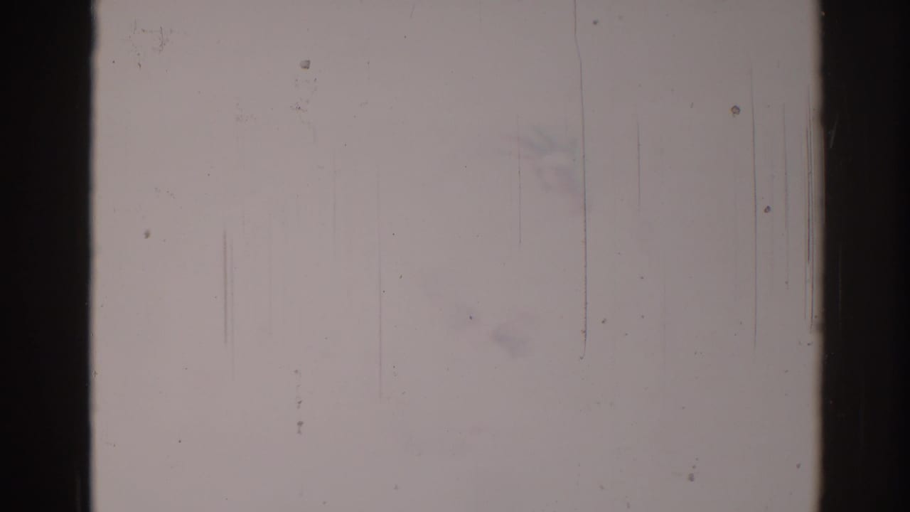 Overexposed 8mm frame with dark vertical film edges, scratches, dust, and very little visible scene detail.