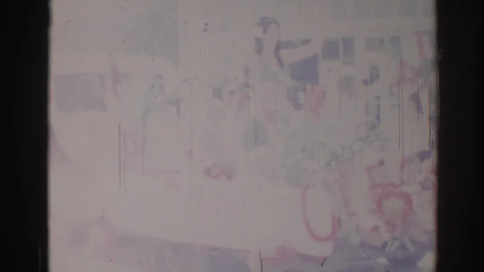 Faded 1967 Los Angeles home-movie frame showing blurred people in green uniforms during a parade, with heavy washout and vertical scratches.