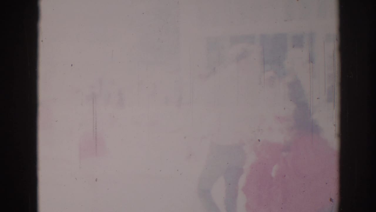 Soft 1967 Los Angeles parade frame with a pink-clad figure near the right edge and faint background shapes through faded 8mm color.