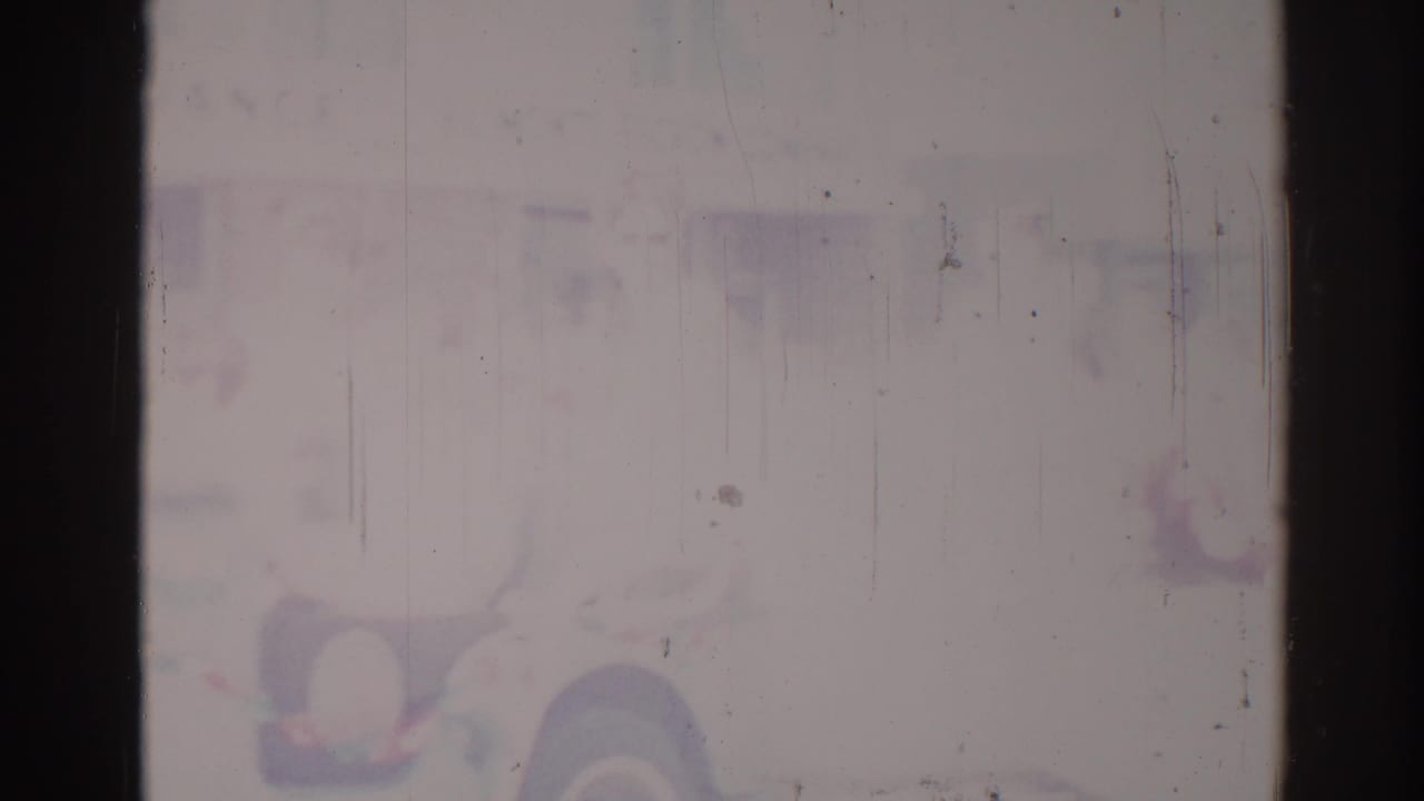 Degraded 1967 Los Angeles 8mm frame with a faint vehicle- or float-like shape and muted purple-blue fading.