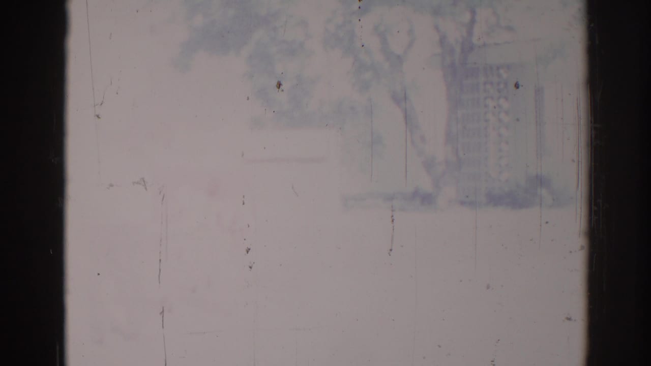 1967 Los Angeles home-movie frame showing a nearly washed-out exterior view with faint tree and building forms and visible 8mm wear.