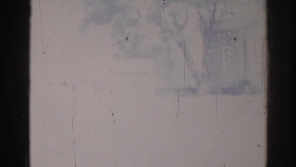 1967 Los Angeles home-movie frame showing a nearly washed-out exterior view with faint tree and building forms and visible 8mm wear.