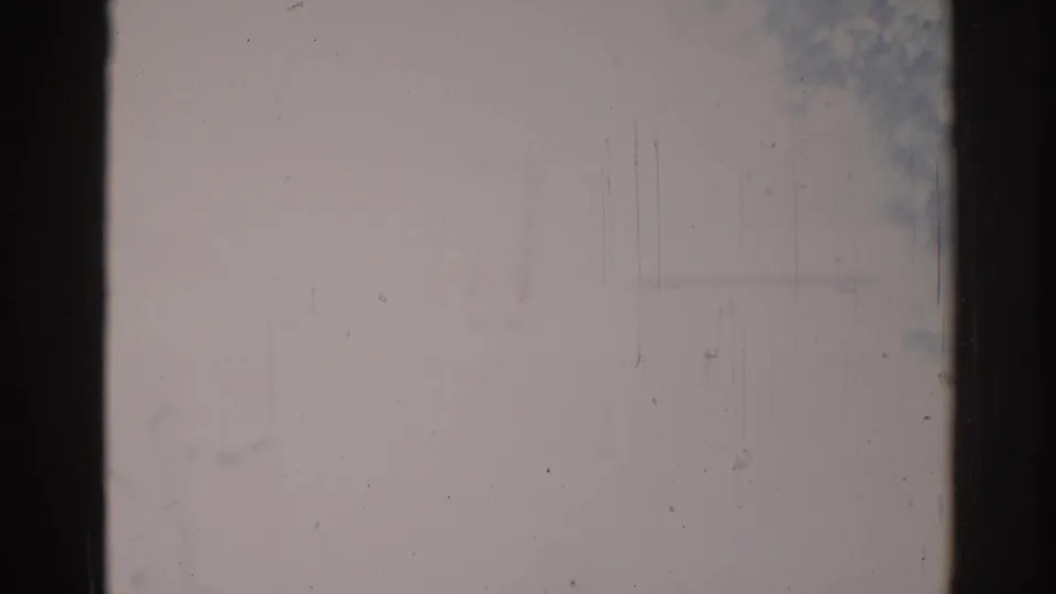 Obscured 1967 Los Angeles 8mm frame with dark borders, pale outdoor tones, scratches, and indistinct street-like forms.