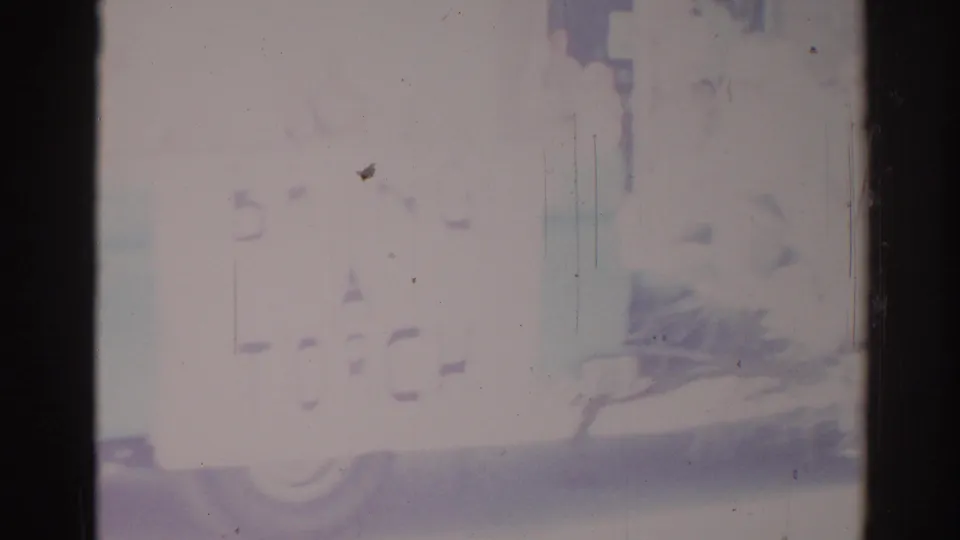 Faded 1967 Los Angeles home-movie frame with possible street or parade forms, dark vertical borders, scratches, and blue-purple discoloration.