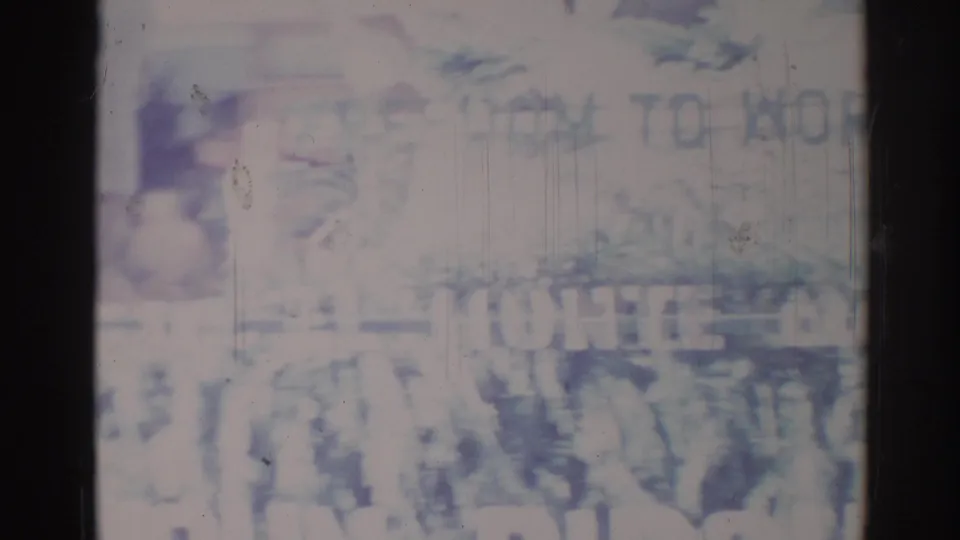 1967 Los Angeles home-movie frame showing a blurry parade scene with large lettering and nearby spectators.