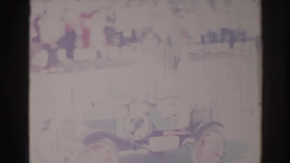 1967 Los Angeles home-movie frame showing an antique-style open car passing through a street parade with spectators in the background.