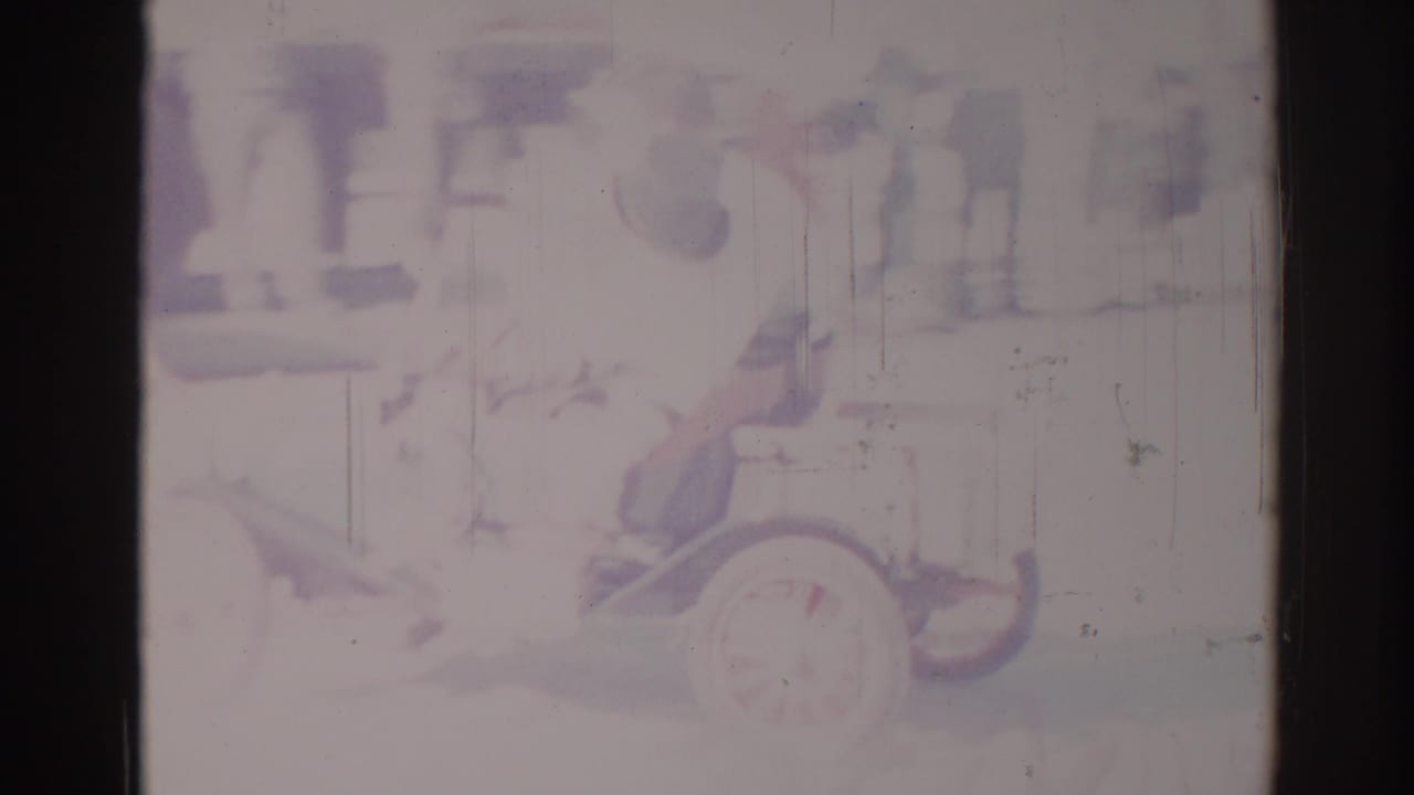 Antique-style car at right with a seated figure and blurred parade activity behind it.