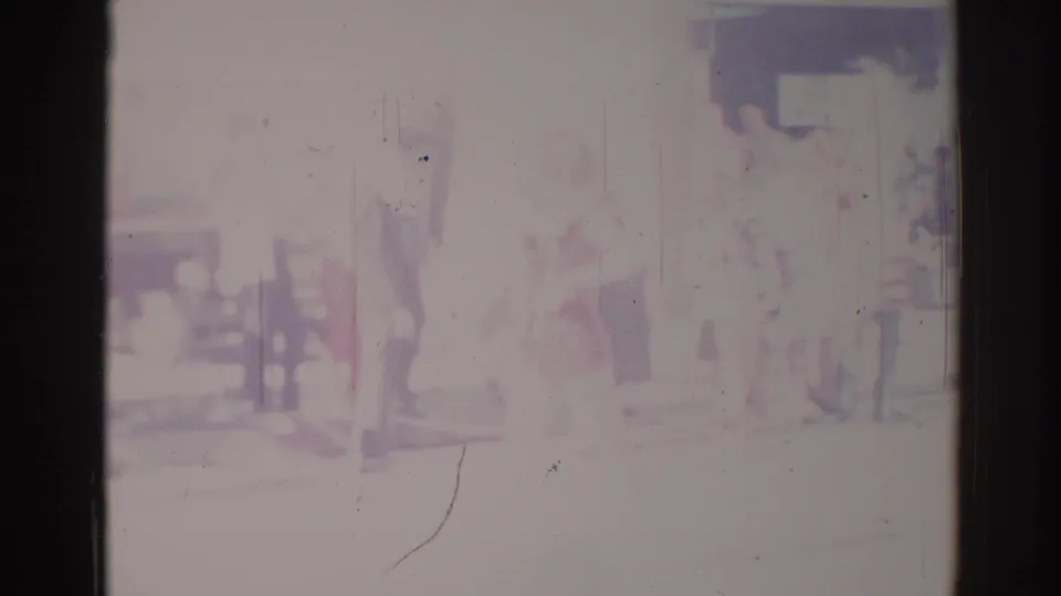 1967 Los Angeles home-movie frame with indistinct parade participants or spectators near the curb and part of a vehicle at right.