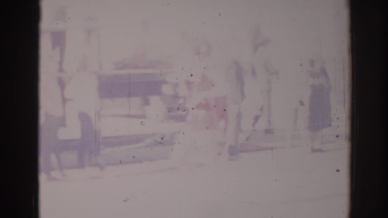 1967 Los Angeles home-movie frame showing a very faded street parade view with blurred figures and a vehicle shape.