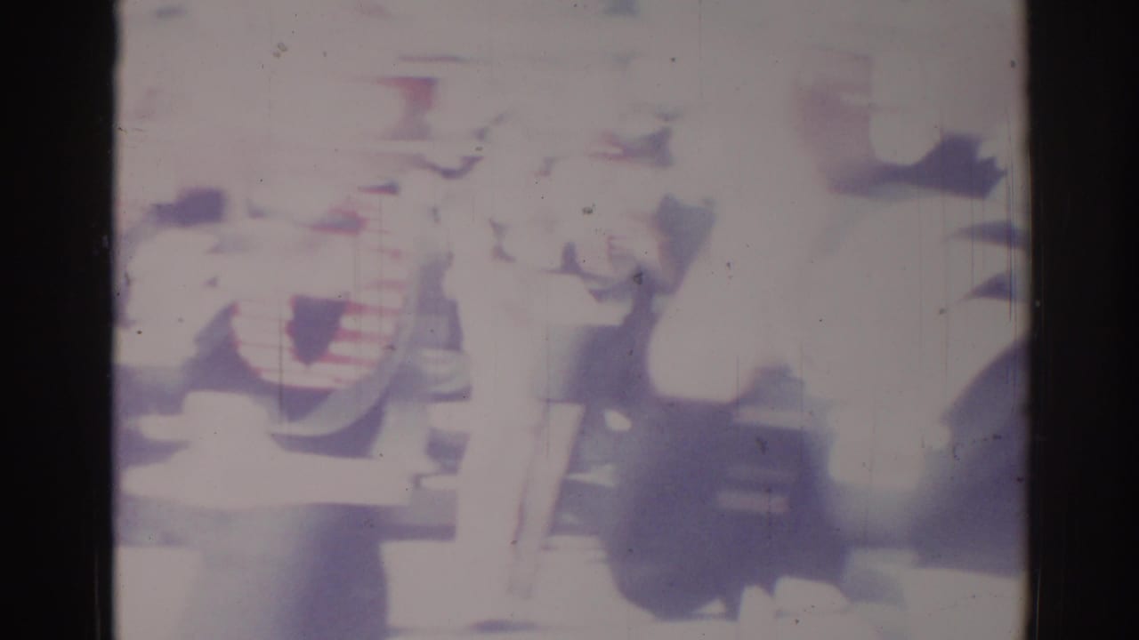 1967 Los Angeles home-movie frame with a blurred person in light clothing near street activity and heavy film fade.