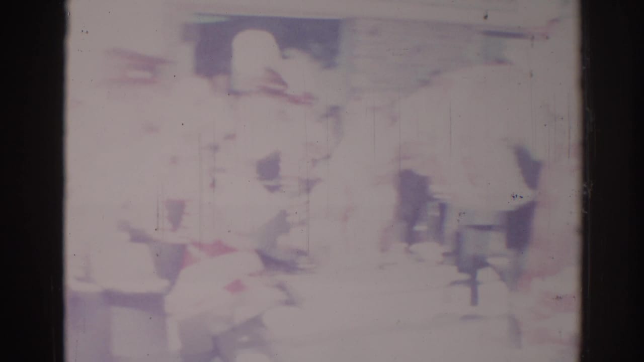 Soft, faded 1967 Los Angeles street-parade frame with several indistinct people along an urban curbside area.