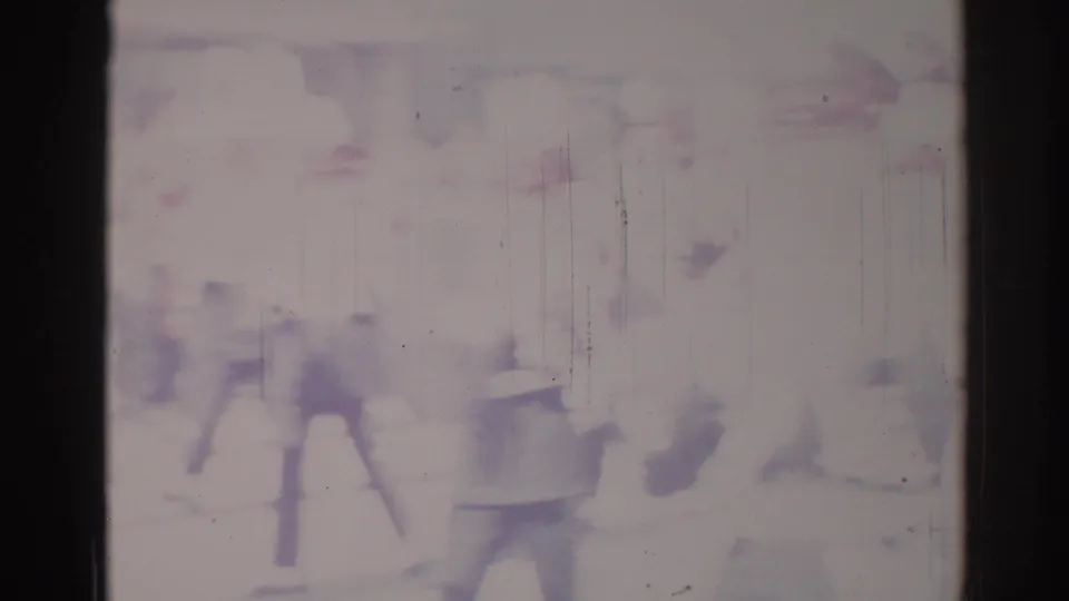 Blurry 1967 Los Angeles 8mm frame showing indistinct people walking near a large sign and street-level building frontage.