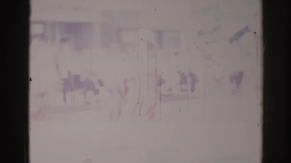 Faded 1967 Los Angeles parade footage shows indistinct people near a pale street-side building, framed by dark 8mm film edges.