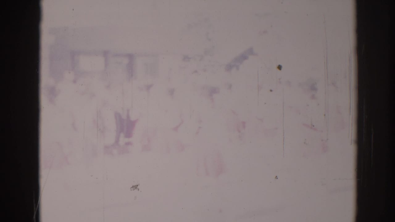 A very washed-out 8mm frame shows faint people at a Los Angeles parade scene, with most detail obscured by fading and scratches.