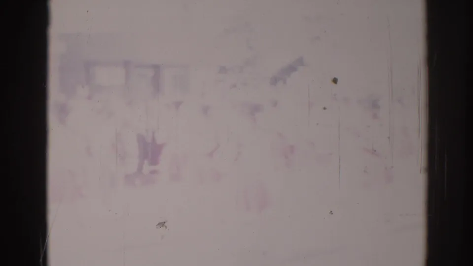 A very washed-out 8mm frame shows faint people at a Los Angeles parade scene, with most detail obscured by fading and scratches.
