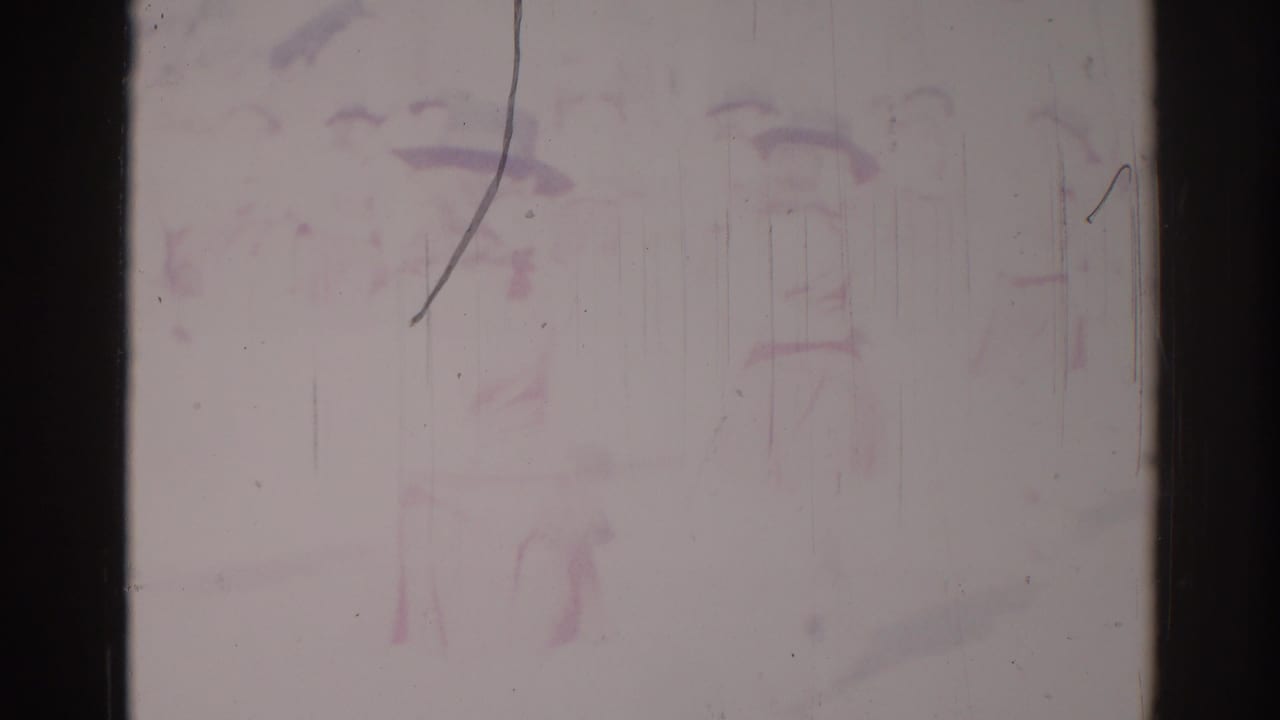 Faded 8mm frame with faint parade figures and heavy vertical scratches.