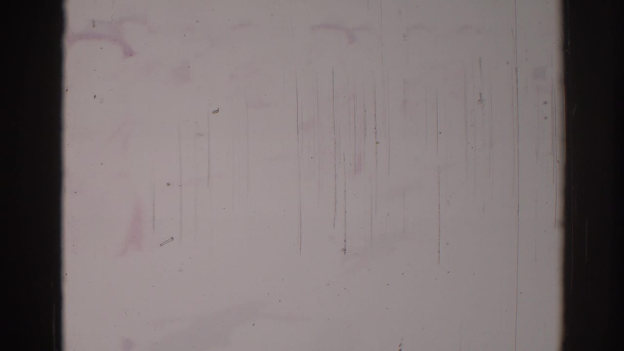 Faded 8mm parade frame with possible people near the lower left, softened by exposure loss, scratches, and dust.