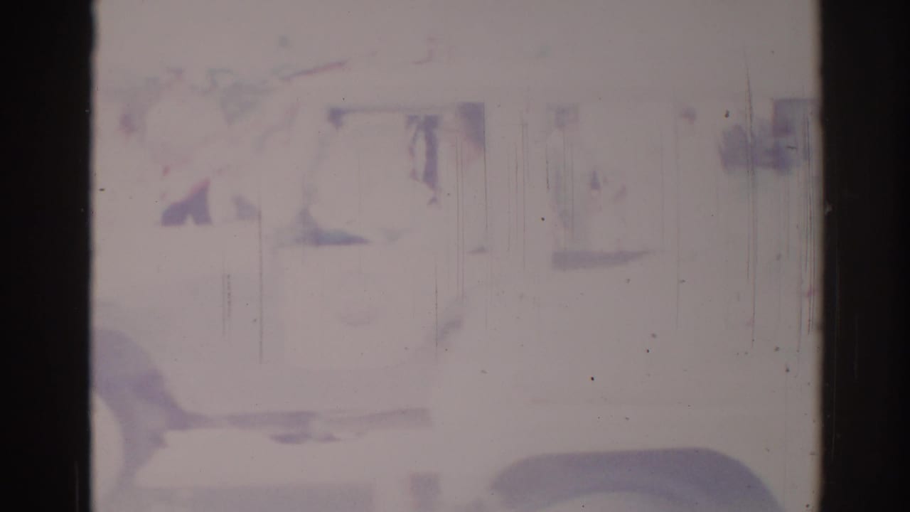 The white truck passes close to camera, with its side and wheel visible through faded 8mm film damage.